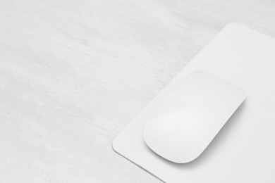 Photo of Computer mouse with mousepad on light wooden table, closeup. Space for text