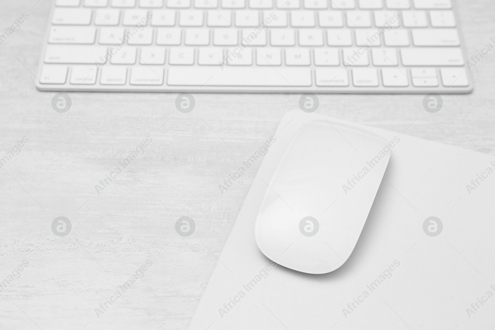 Photo of Computer mouse with mousepad and keyboard on light wooden table, closeup. Space for text