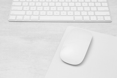 Photo of Computer mouse with mousepad and keyboard on light wooden table, closeup. Space for text