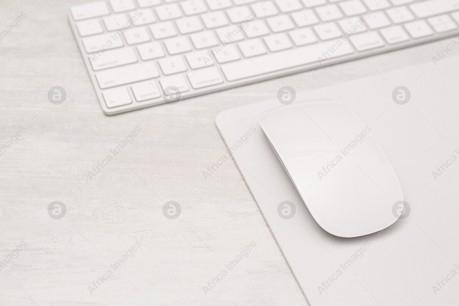 Photo of Computer mouse with mousepad and keyboard on light wooden table, closeup. Space for text