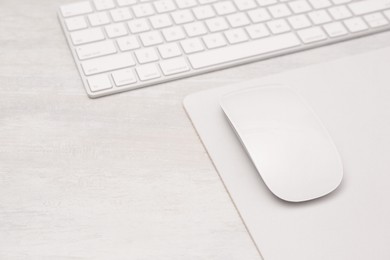 Photo of Computer mouse with mousepad and keyboard on light wooden table, closeup. Space for text