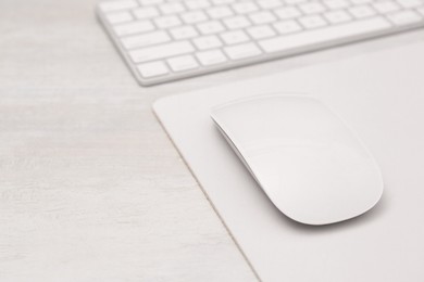 Photo of Computer mouse with mousepad and keyboard on light wooden table, closeup. Space for text