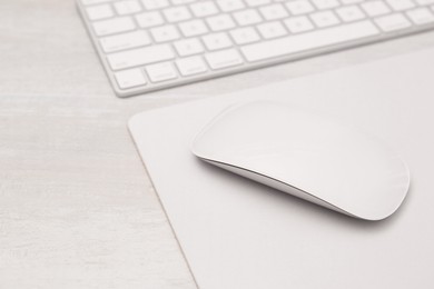 Photo of Computer mouse with mousepad and keyboard on light wooden table, closeup