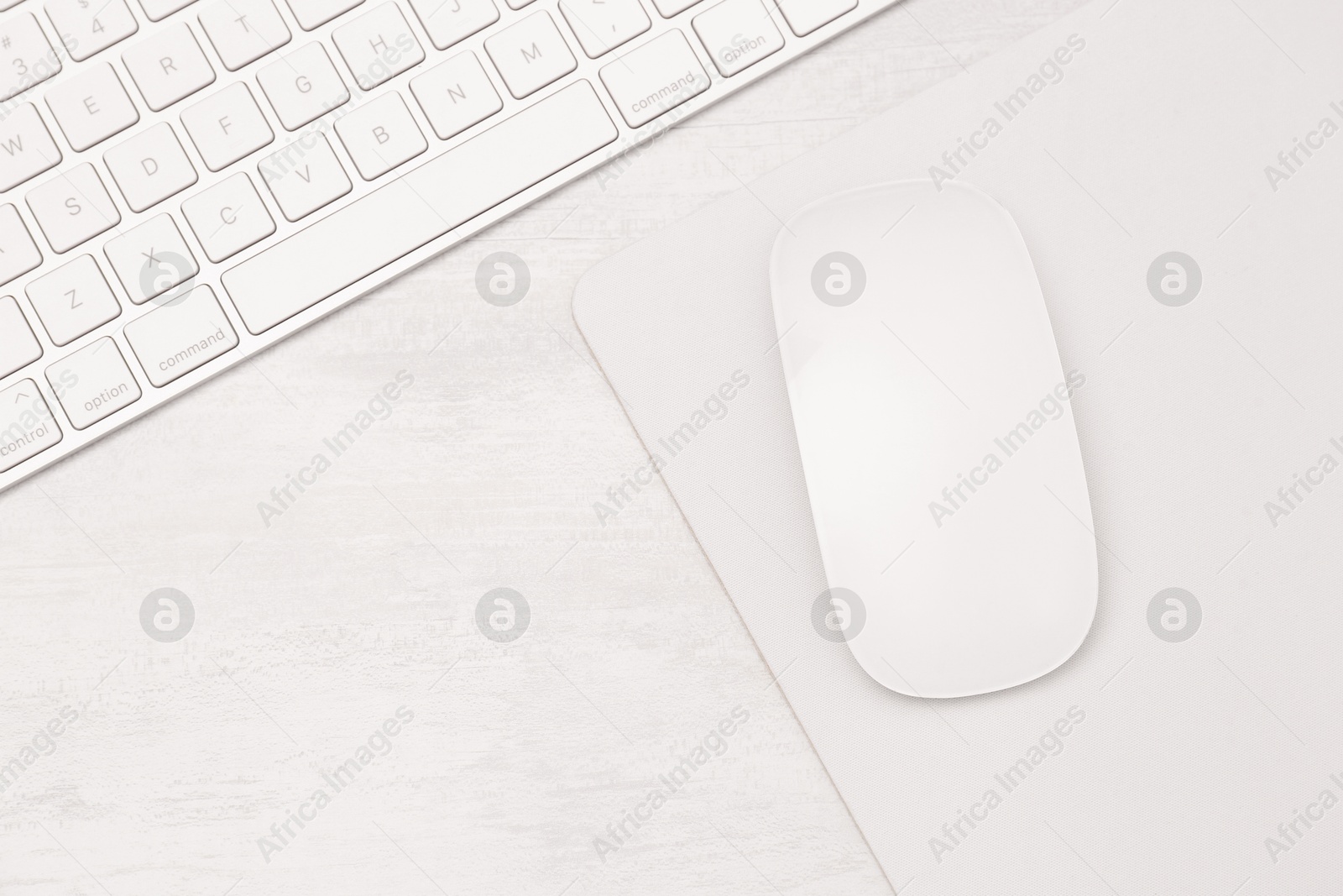 Photo of Computer mouse with mousepad and keyboard on light wooden table, flat lay. Space for text