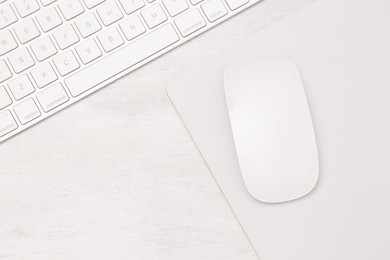 Photo of Computer mouse with mousepad and keyboard on light wooden table, flat lay. Space for text