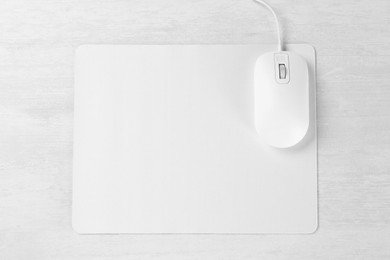 Photo of Computer mouse with mousepad on light wooden table, top view