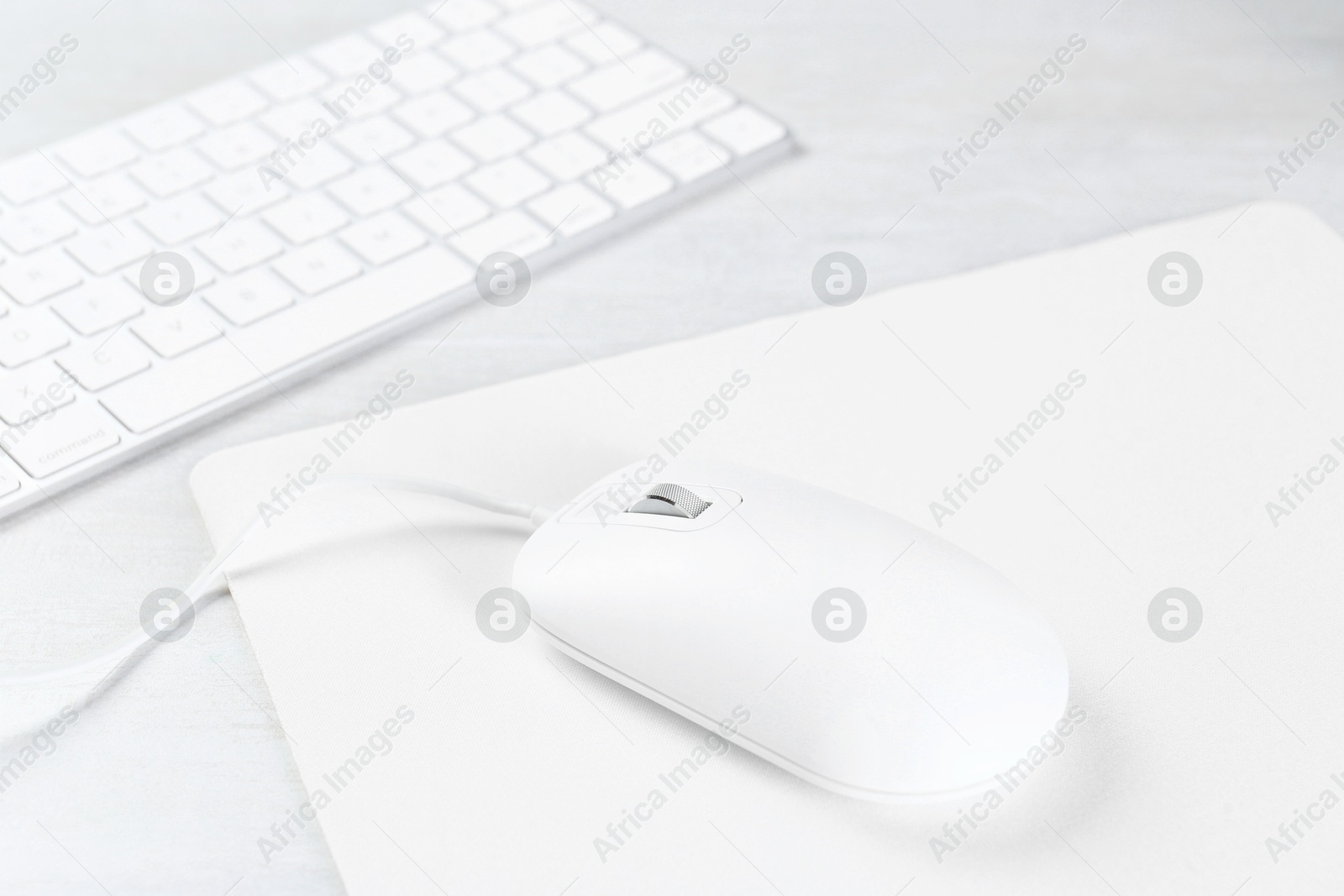 Photo of Computer mouse with mousepad and keyboard on light wooden table, closeup