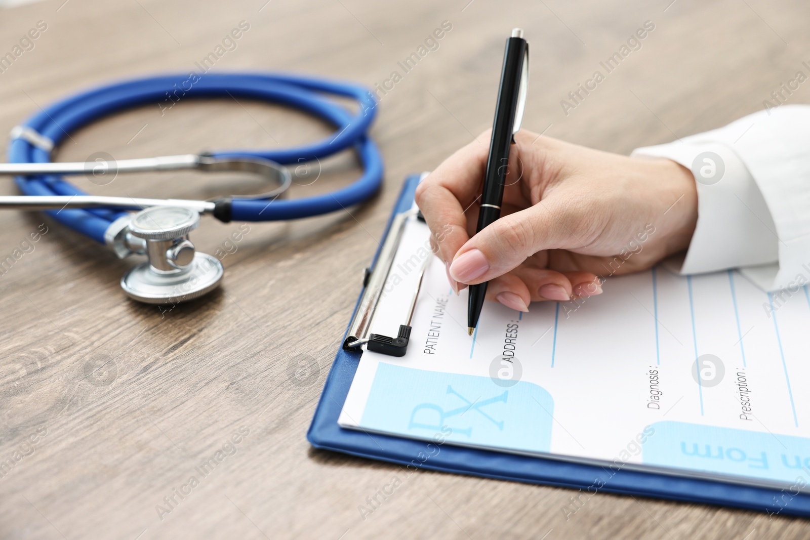 Photo of Doctor writing prescription at wooden table in clinic, closeup