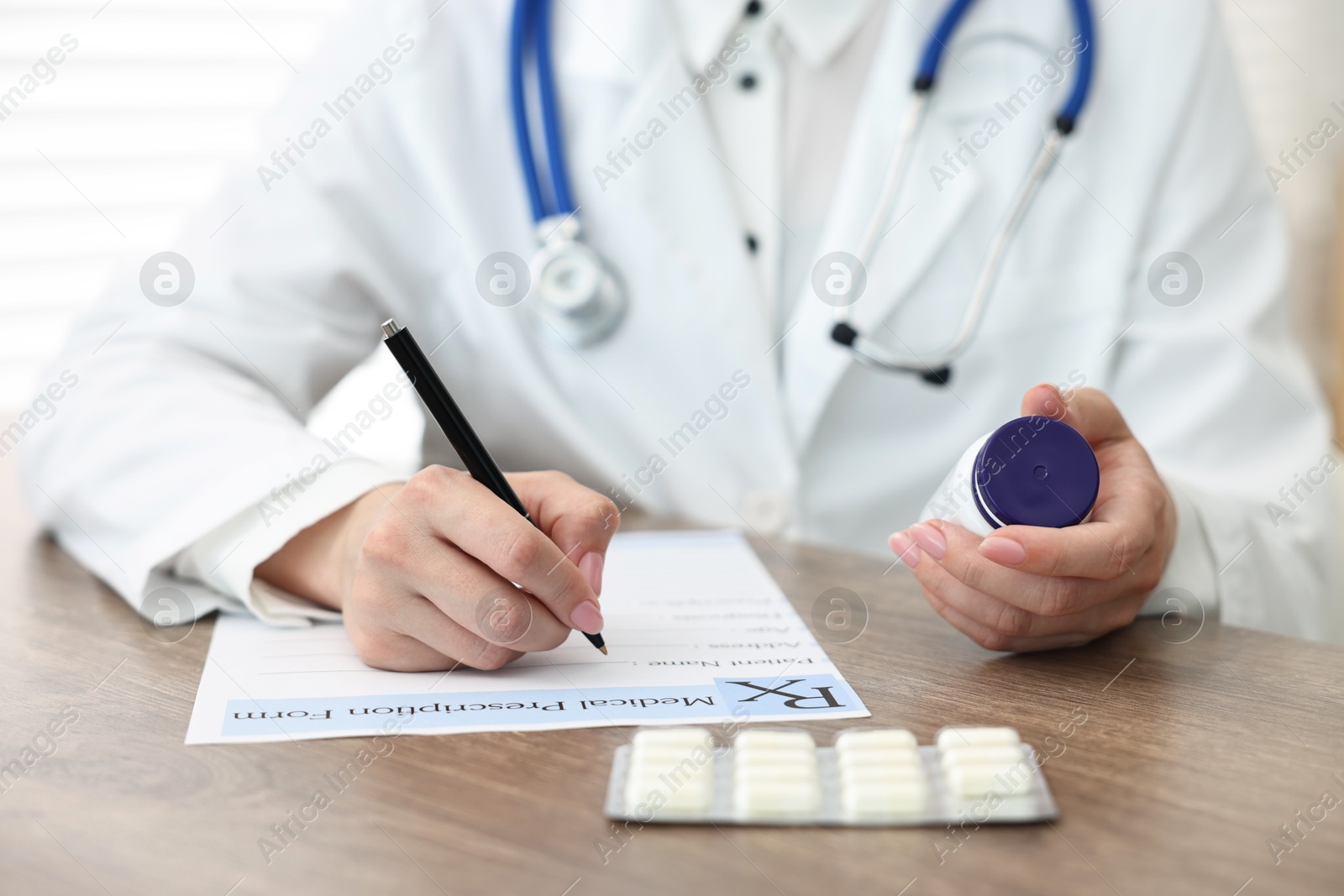 Photo of Doctor with pills writing prescription at wooden table in clinic, closeup