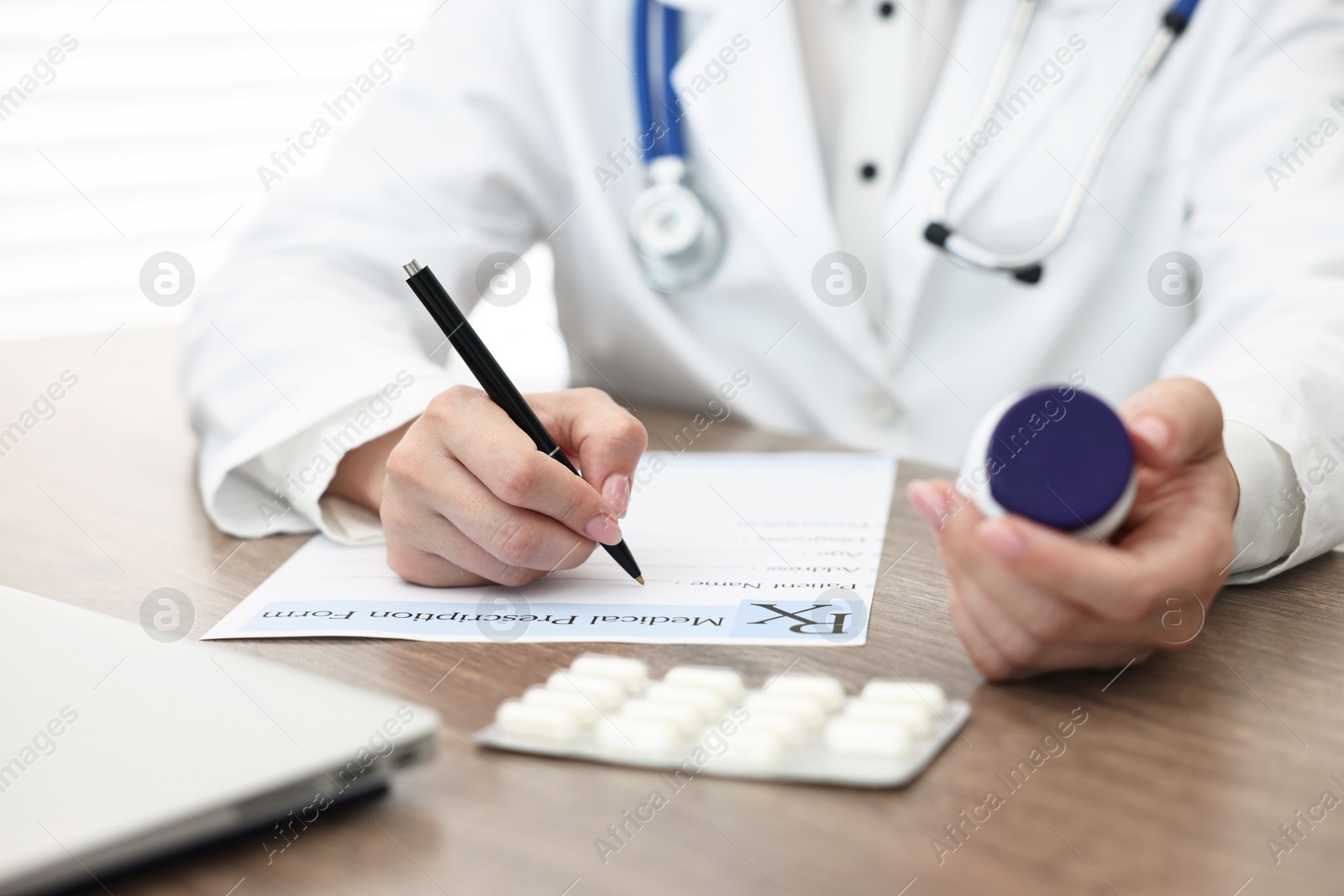 Photo of Doctor with pills writing prescription at wooden table in clinic, closeup