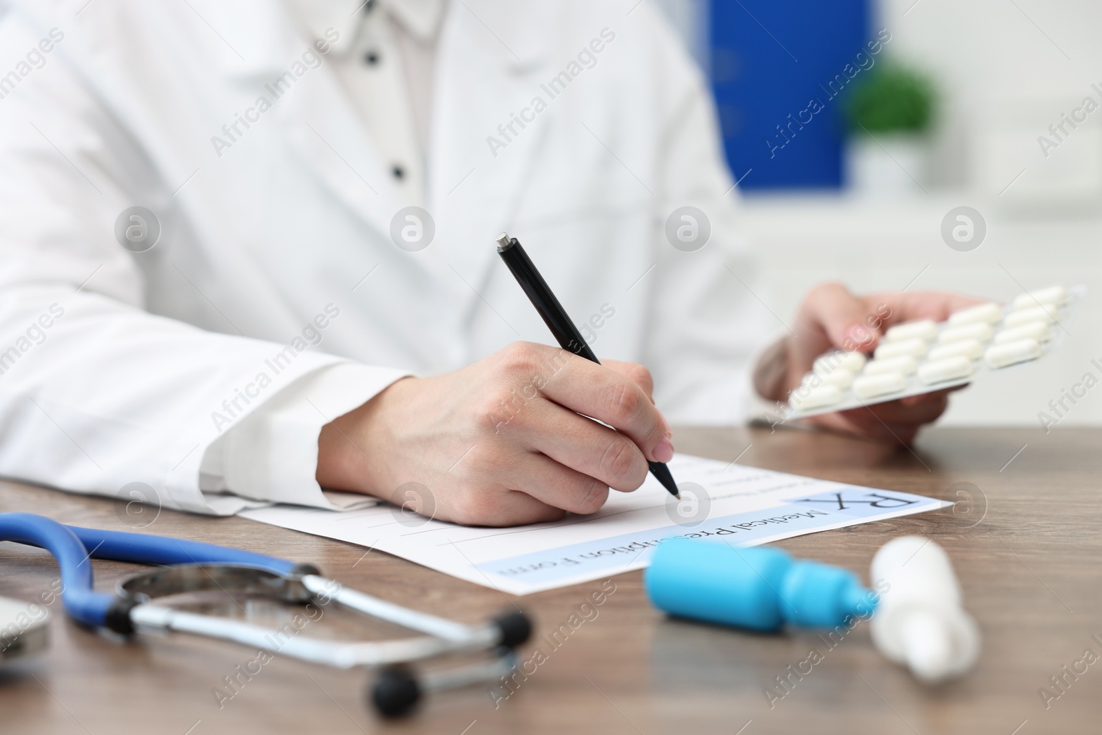 Photo of Doctor with pills writing prescription at wooden table in clinic, closeup