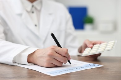 Photo of Doctor with pills writing prescription at wooden table in clinic, closeup