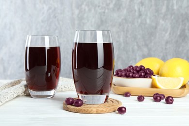 Photo of Tasty fresh acai juice in glasses with berries and lemons on white wooden table