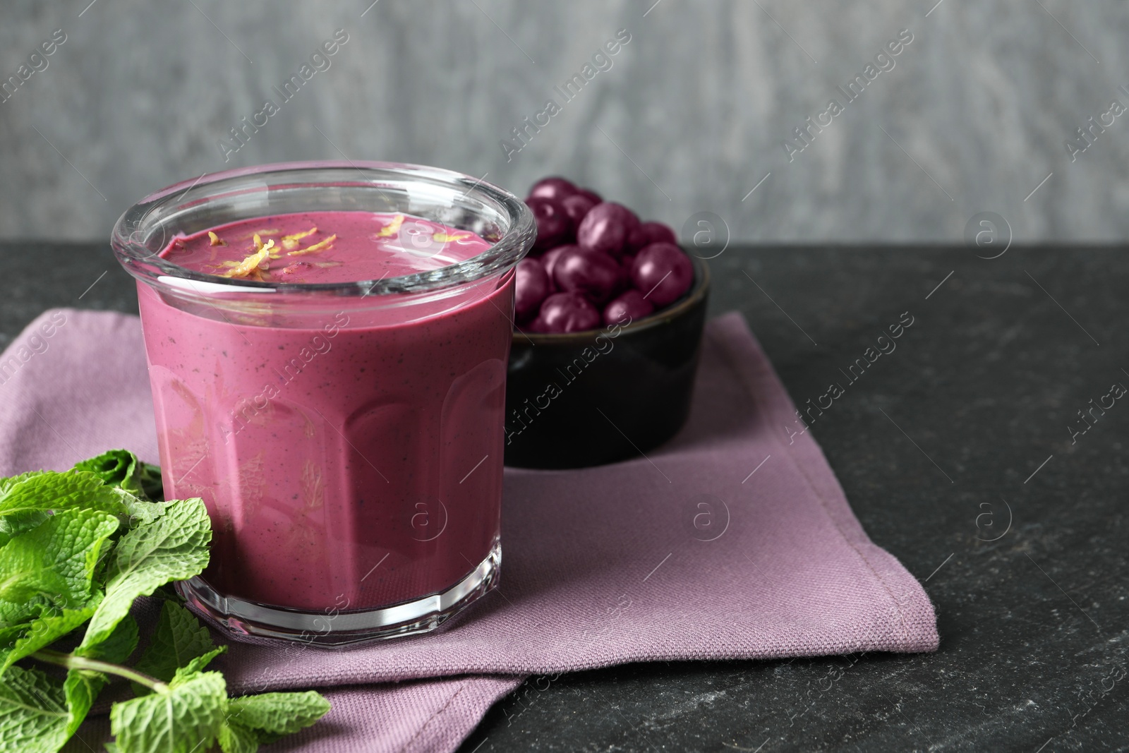 Photo of Tasty fresh acai juice in glass with mint and berries on grey textured table, space for text