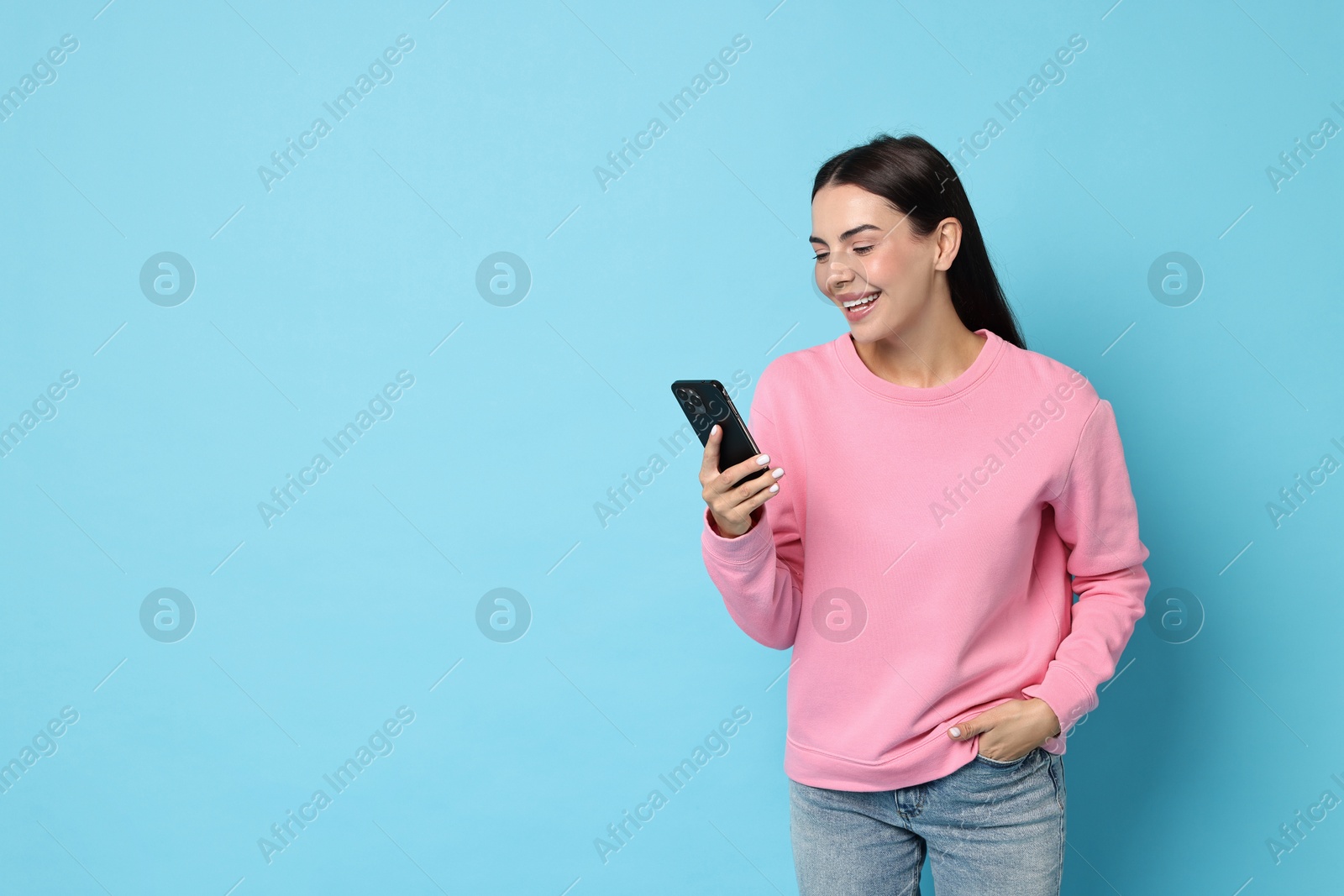 Photo of Smiling woman with smartphone on light blue background. Space for text