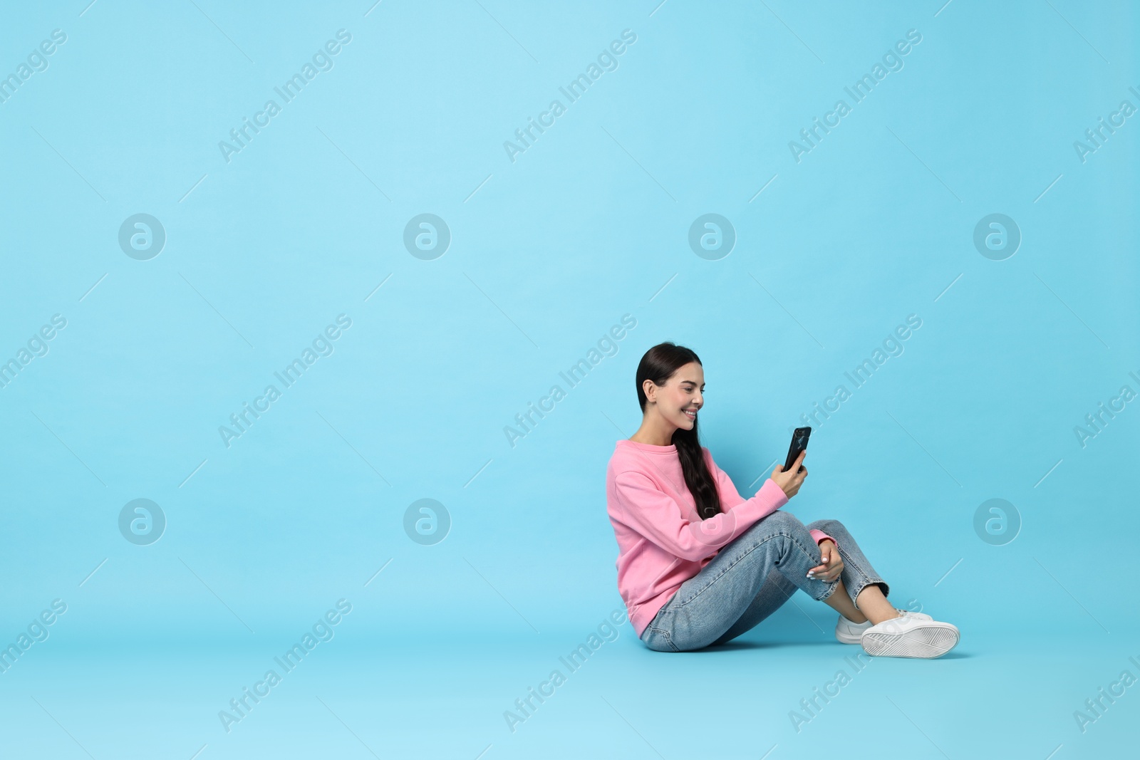 Photo of Smiling woman with smartphone on light blue background. Space for text