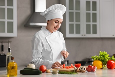 Professional chef cutting tomato at table in kitchen