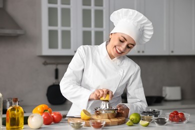 Woman squeezing juice out of lemon at table in kitchen