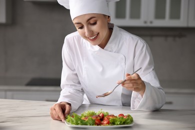 Photo of Professional chef adding sauce to dish with baked chicken at white marble table in kitchen