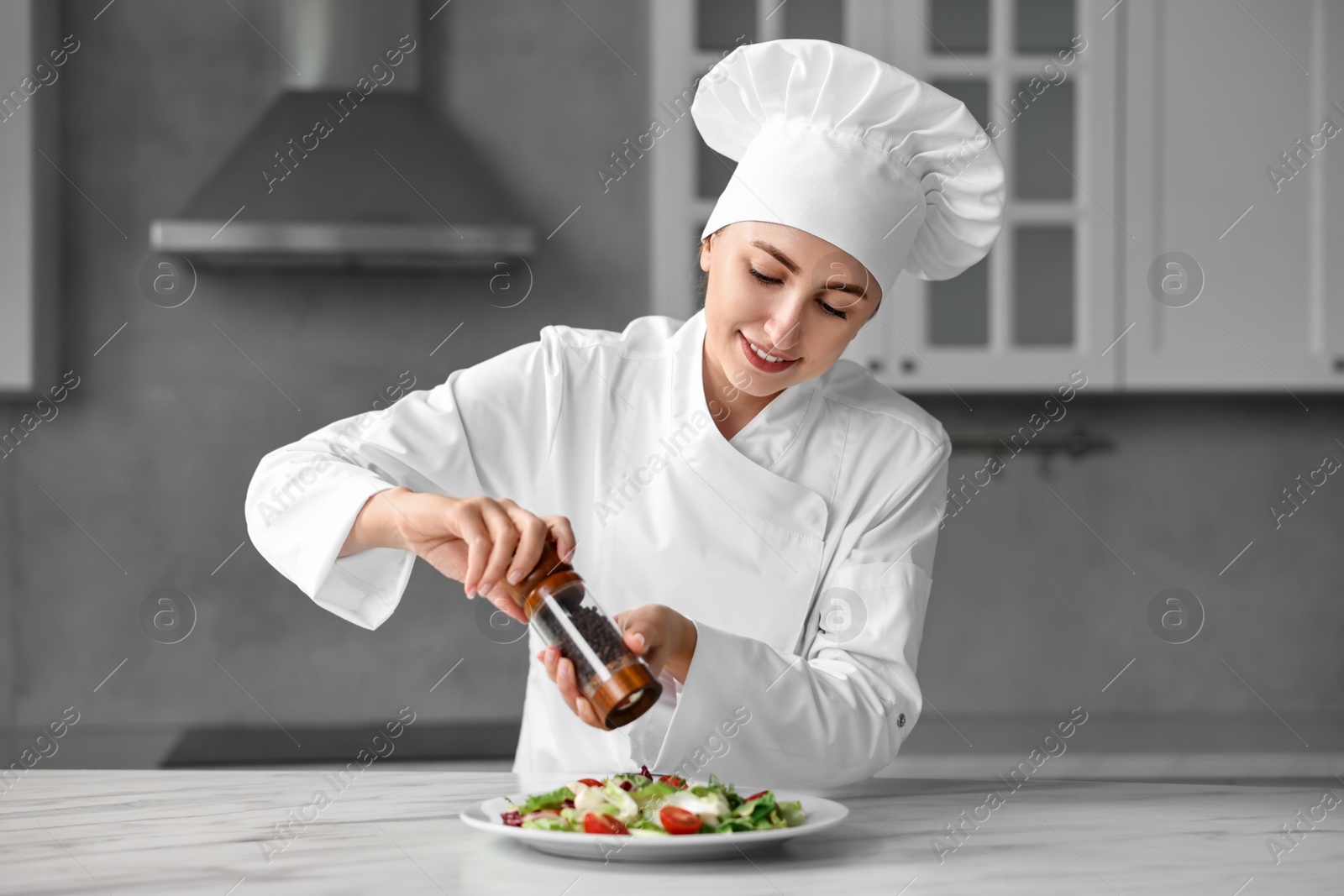 Photo of Professional chef adding pepper to delicious salad at white marble table in kitchen