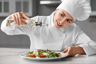 Professional chef pouring oil onto delicious salad at white marble table in kitchen