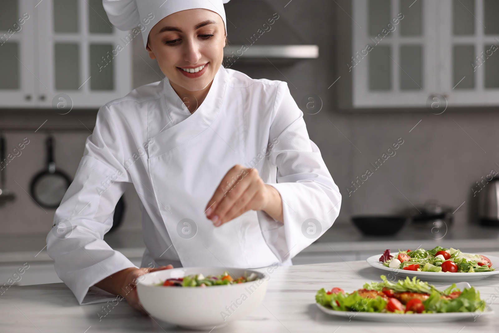 Photo of Professional chef adding salt to delicious salad at white marble table in kitchen