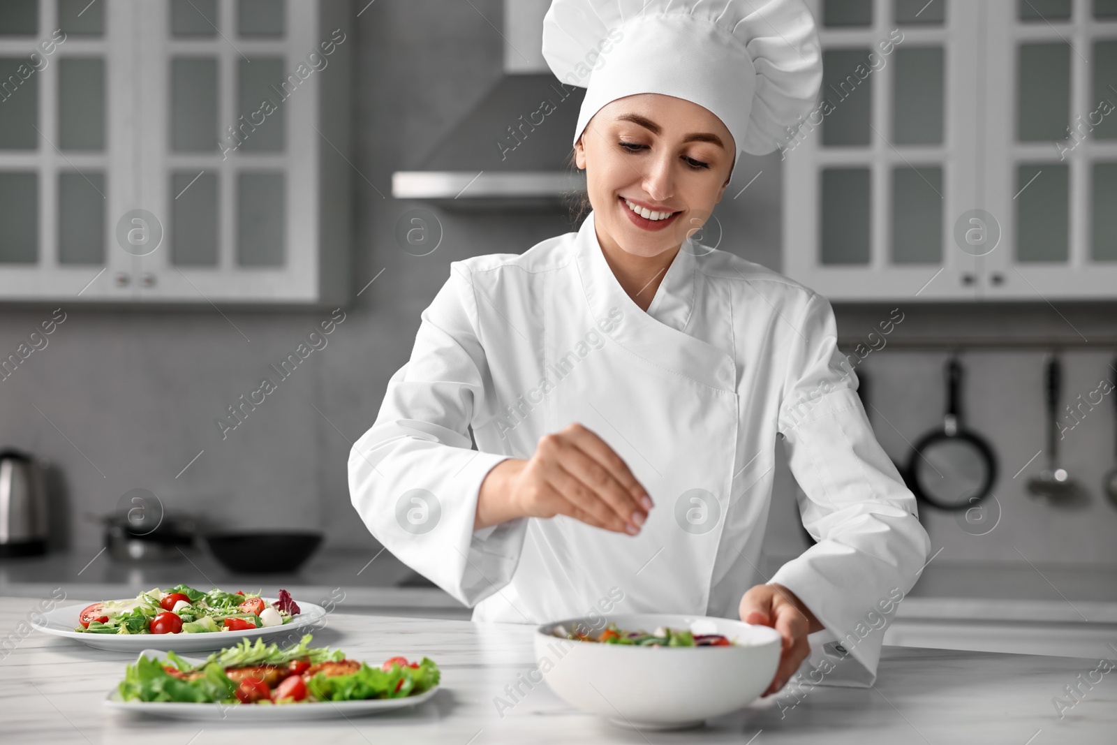 Photo of Professional chef adding salt to delicious salad at white marble table in kitchen