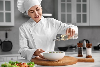 Photo of Professional chef pouring oil onto delicious salad at table in kitchen