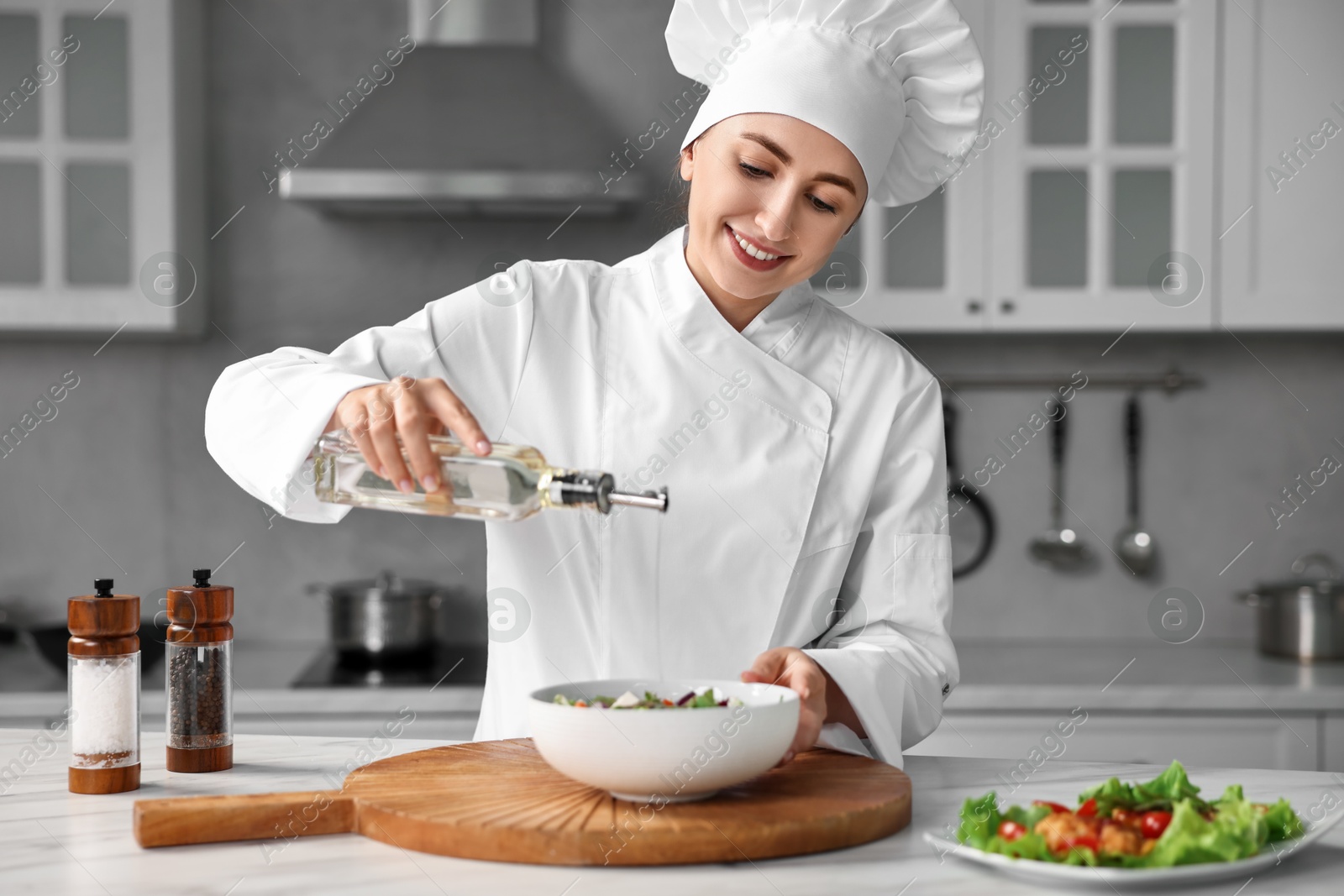 Photo of Professional chef pouring oil onto delicious salad at table in kitchen