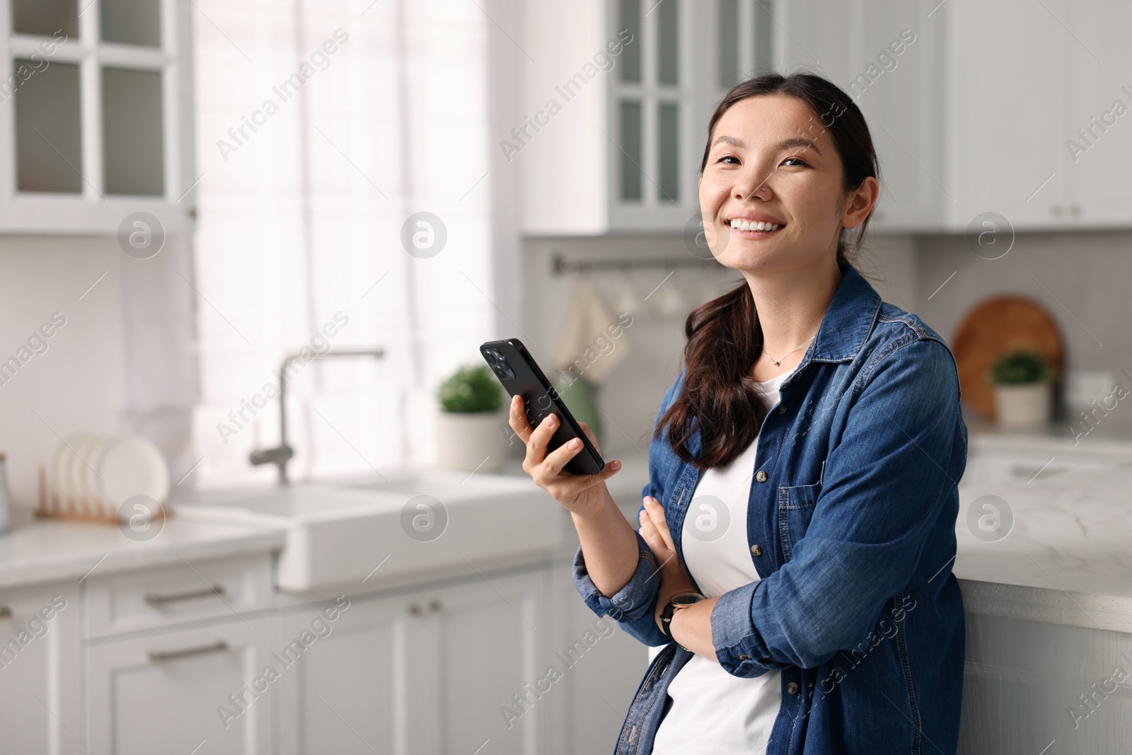 Photo of Smiling woman with smartphone in kitchen. Space for text