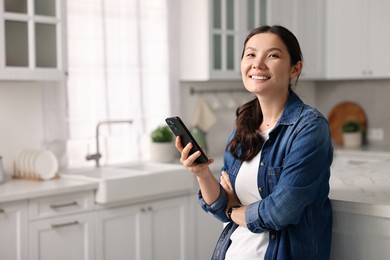 Photo of Smiling woman with smartphone in kitchen. Space for text