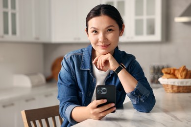 Photo of Portrait of beautiful woman with smartphone in kitchen