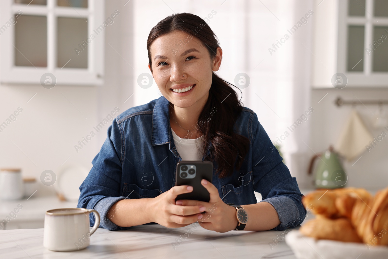 Photo of Portrait of smiling woman with smartphone in kitchen