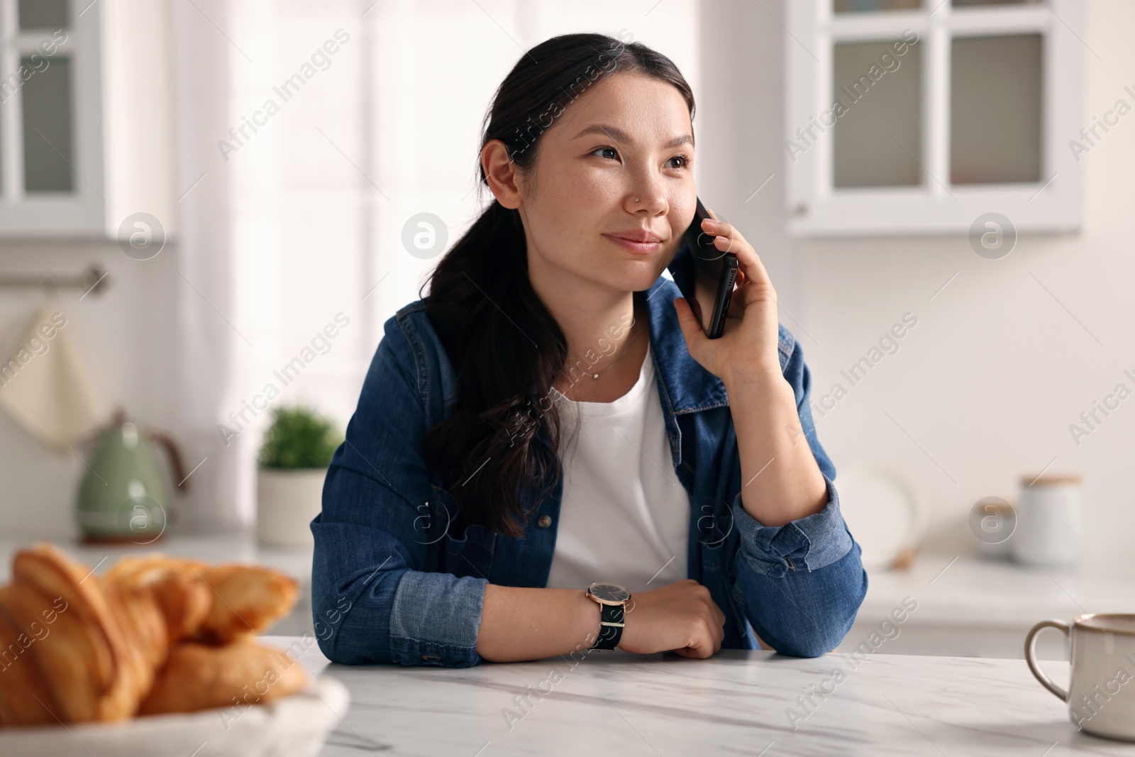 Photo of Beautiful woman talking on smartphone in kitchen