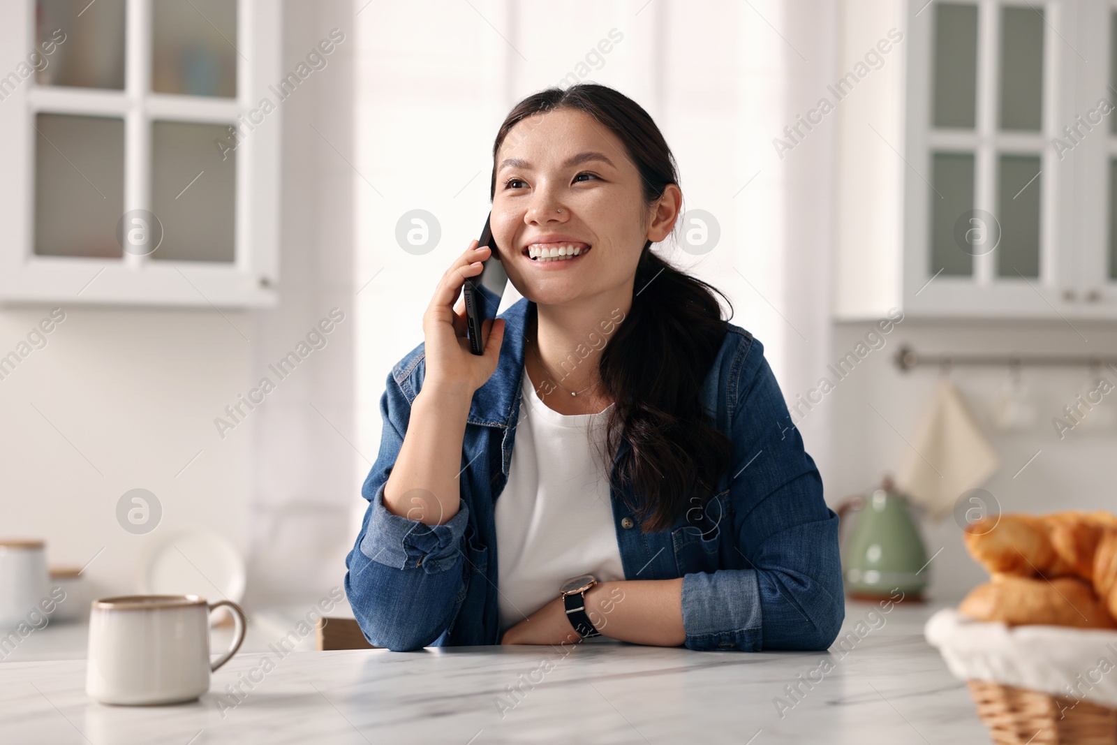 Photo of Smiling woman talking on smartphone in kitchen