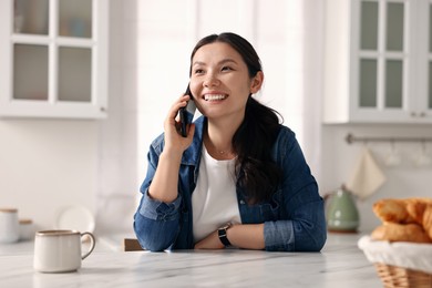 Smiling woman talking on smartphone in kitchen