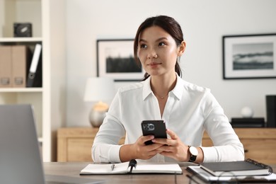 Beautiful businesswoman with smartphone at table in office