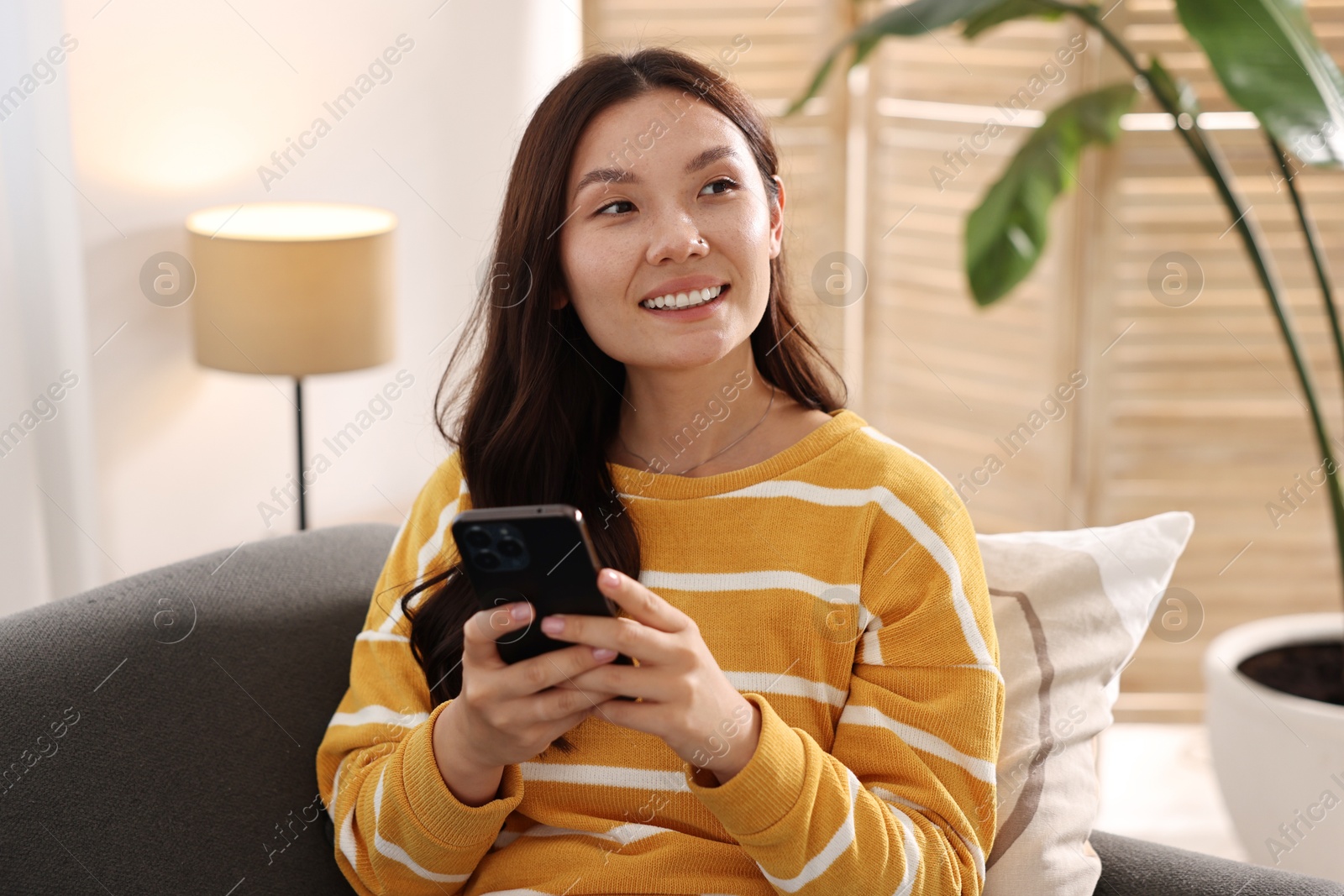 Photo of Portrait of smiling woman with smartphone at home