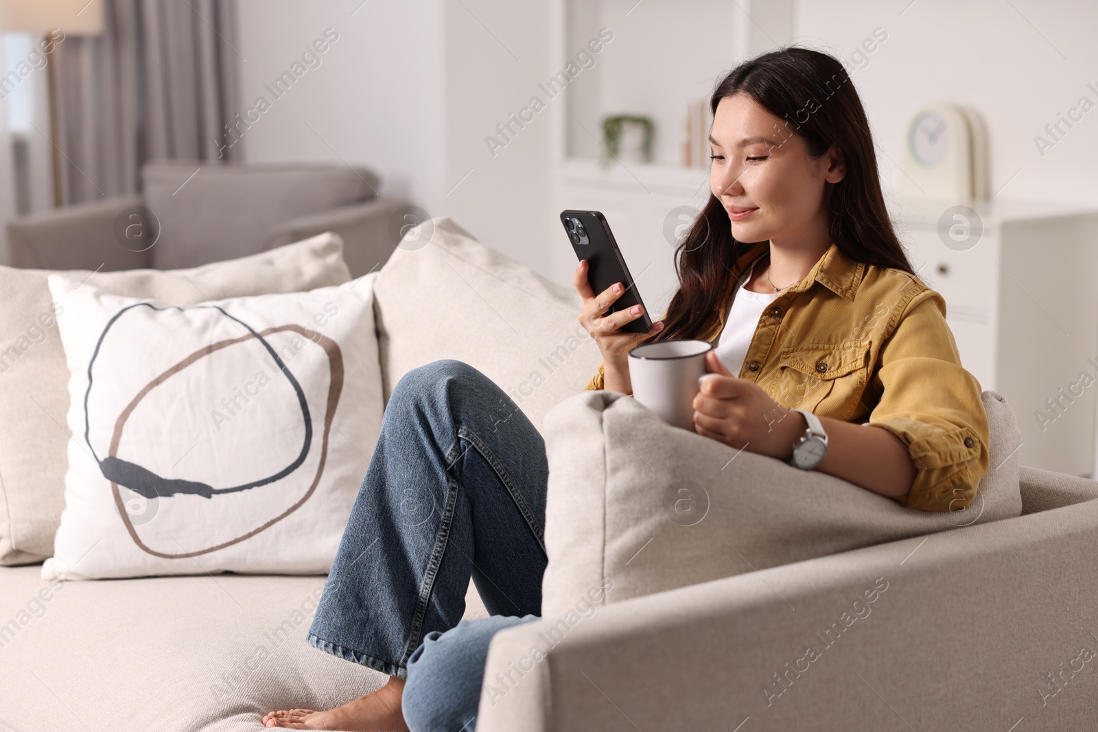 Photo of Beautiful woman with smartphone and cup on sofa at home