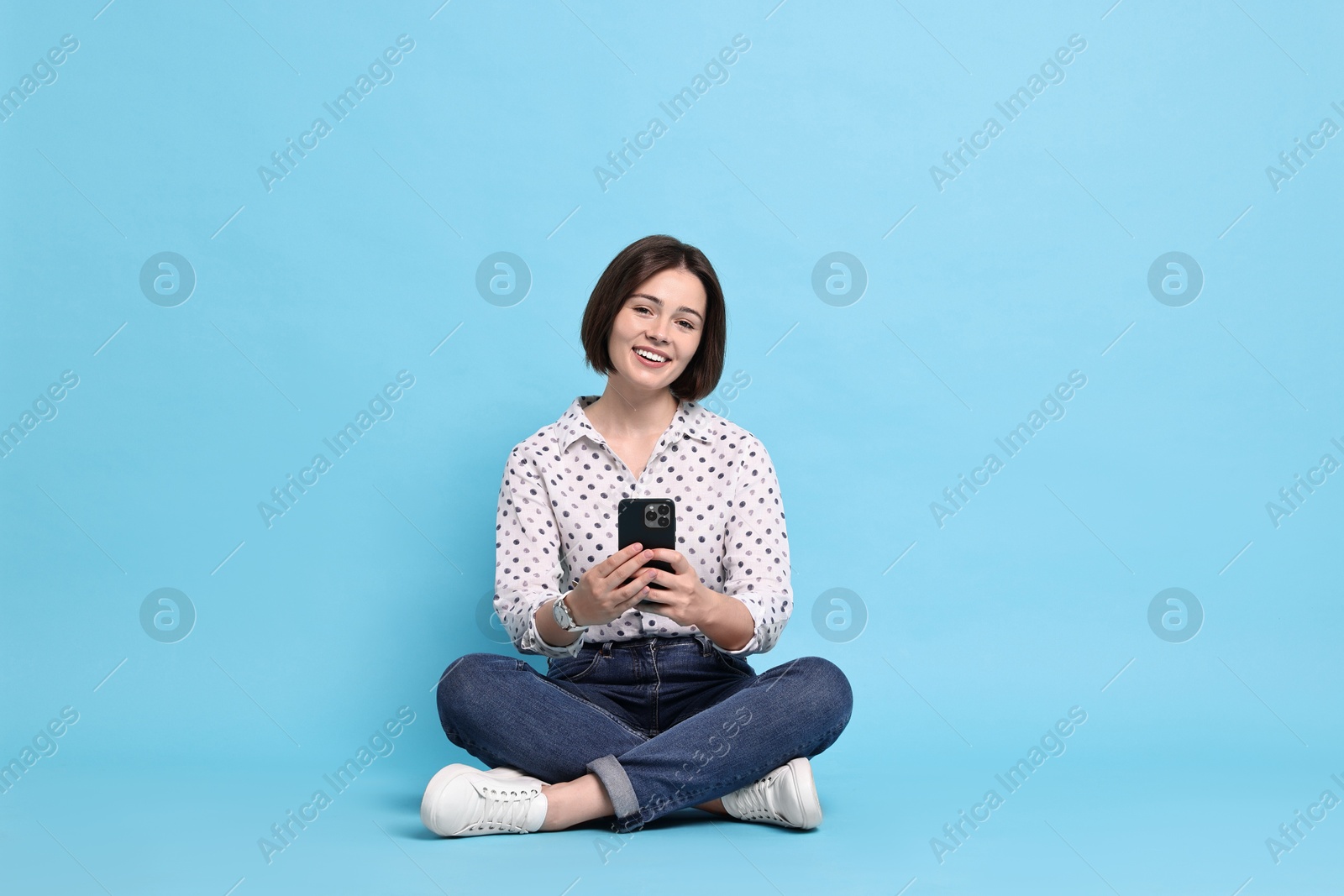 Photo of Smiling woman with smartphone sitting on light blue background