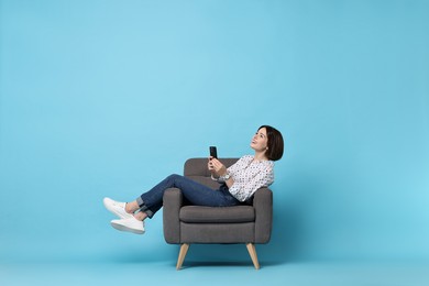 Photo of Smiling woman with smartphone resting on armchair against light blue background