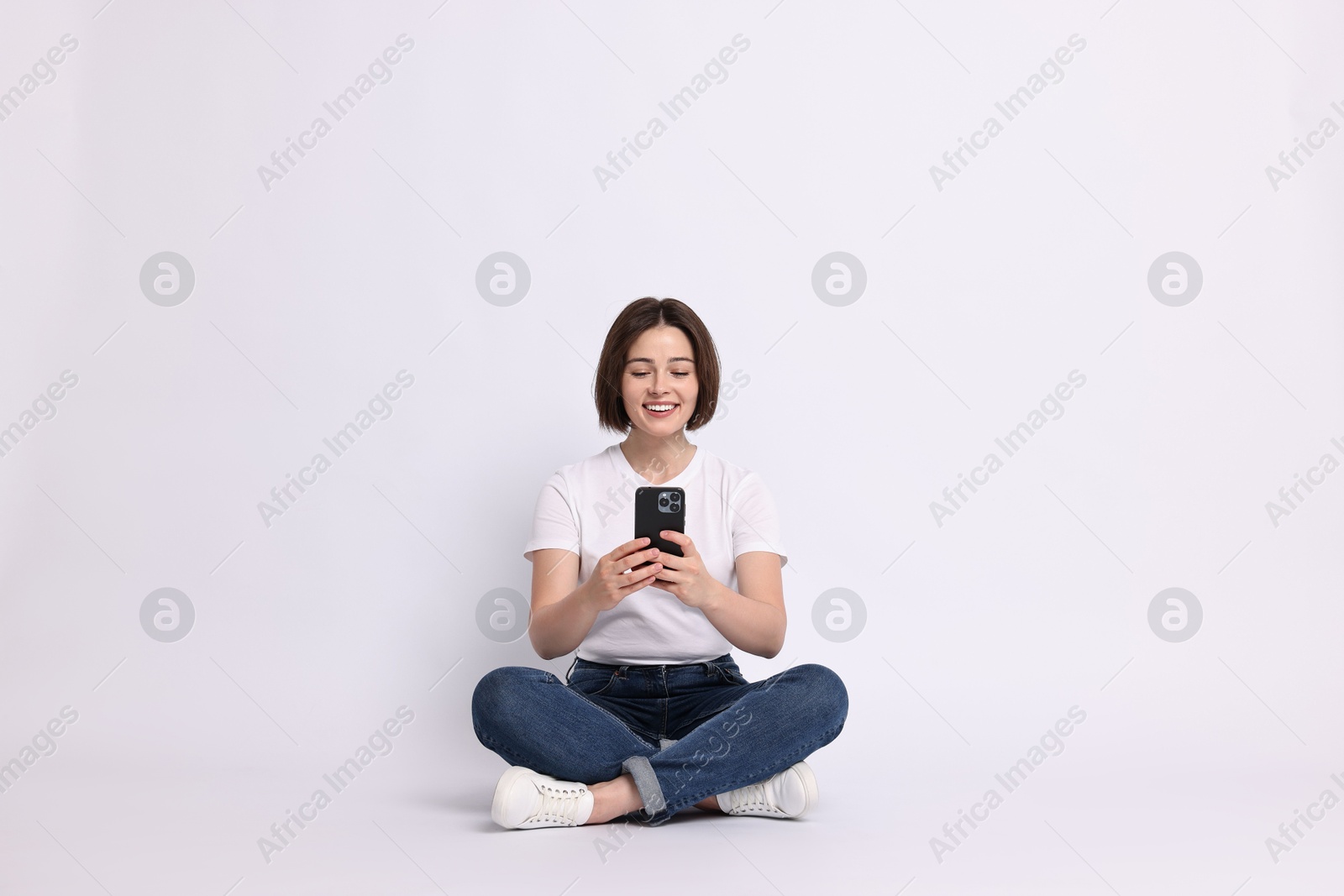 Photo of Smiling woman with smartphone sitting on white background