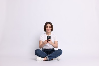 Smiling woman with smartphone sitting on white background