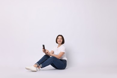 Photo of Smiling woman with smartphone sitting on white background. Space for text