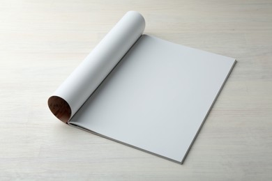 Open magazine with blank page on light wooden table. Mockup for design