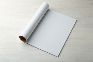 Open magazine with blank page on light wooden table. Mockup for design