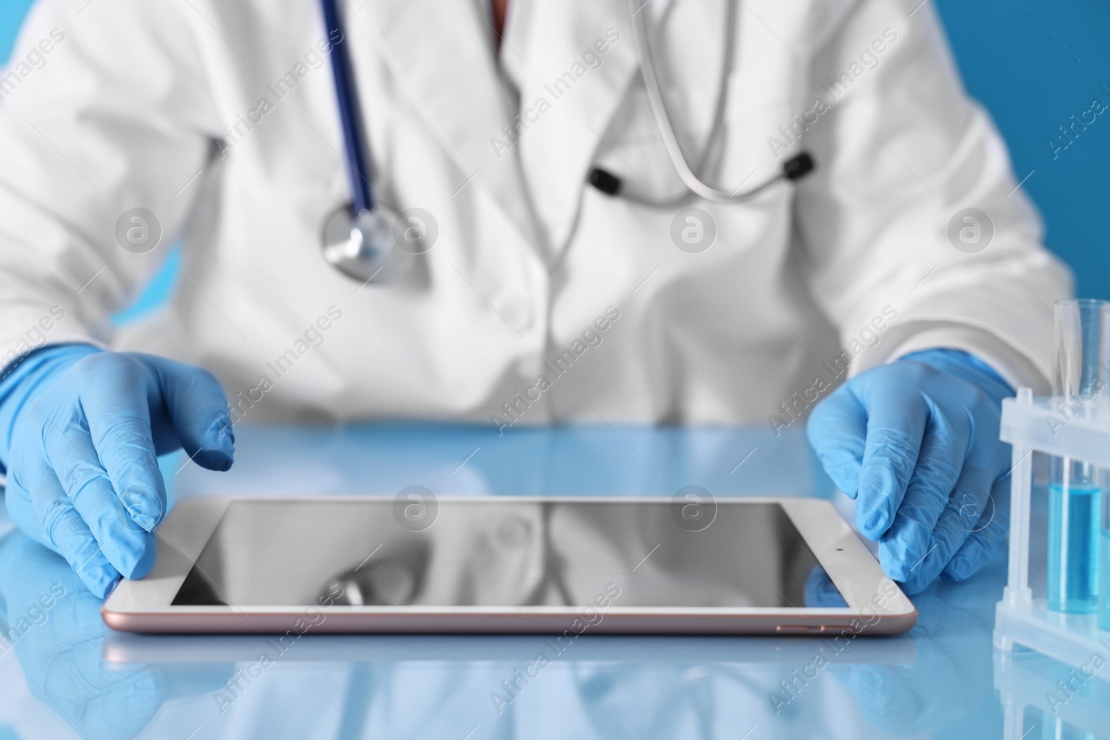 Photo of Doctor with tablet at table against light blue background, closeup view