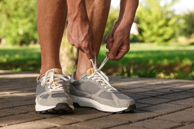 Photo of Man tying shoelace of grey sneaker outdoors, closeup