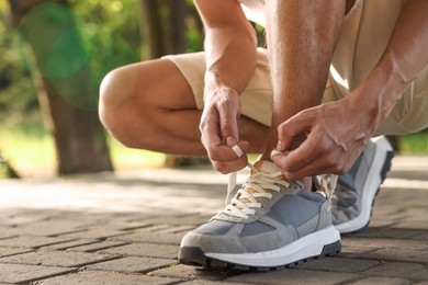 Man tying shoelace of grey sneaker outdoors, closeup