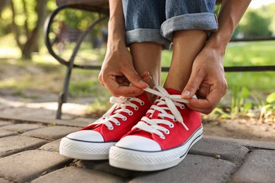 Photo of Woman tying shoelace of red sneaker outdoors, closeup